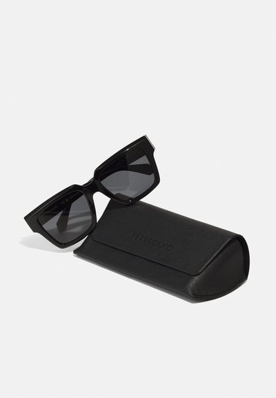 Occhiali da sole neri con una montatura spessa e angolare e lenti scure, posizionati accanto a un astuccio rettangolare nero con texture e marchio in rilievo.