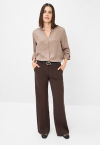 Brown wide-leg trousers paired with a light brown satin blouse featuring a V-neck and puffed sleeves, complemented by a black belt.
