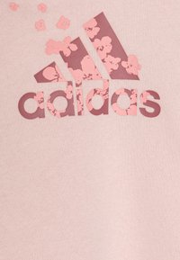 Felpa rosa chiaro con un logo Adidas testurizzato di colore rosa scuro, decorato con motivi floreali e dettagli. È visibile la morbidezza del tessuto.