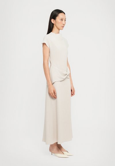 Beige, knee-length dress with short sleeves, featuring a draped front detail. The fabric has a smooth texture. Paired with pointed mules.