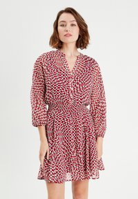Robe à motifs rouges et blancs avec un décolleté en V, des manches longues et une taille élastique. Le tissu est léger et transparent, avec un design à carreaux ondulés.