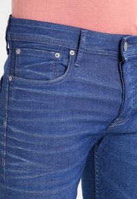 Mörkblå denimjeans med en lätt blekning, utrustade med fem fickor, silverdetaljer och kontrasterande sömmar. Sl ät textur.