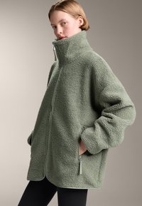 Fleecejack in lichtgroen, met een hoge kraag, ritssluiting en zijzakken. Zacht, gestructureerd stof met een relaxed fit.