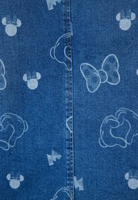 Tejido de mezclilla con estampados en azul claro de cabezas de ratones de dibujos animados, lazos y guantes dispuestos alrededor de una costura central.