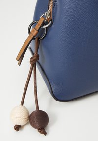 Sac en cuir bleu avec une finition texturée, présentant des accents en tricot marron et crème ainsi qu'un détail de sangle beige. Fermeture éclair avec quincaillerie en métal.