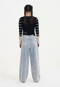 Top a maniche lunghe nera con strisce grigie e una sfumatura sbiadita, abbinato a jeans leggeri blu chiaro larghi con ricami floreali sulla gamba.
