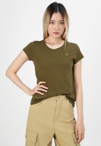 Olive spalvos prigludusi marškinėliai su V-formos iškirpimu ir trumpomis rankovėmis. Audinys atrodo lygus, viršutinėje kairėje krūtinės pusėje yra mažas logotipo elementas.