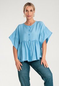 Jasnoniebieska bluzka z guzikami o luźnym kroju, z krótkim rękawem i marszczoną talią. Wykonana z miękkiego, teksturowanego materiału.