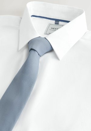 Valge särgikaelusega kleidisärk, millele on sobitatud helesinine tekstuuriga lips. Kaeluses on tikitud silt.