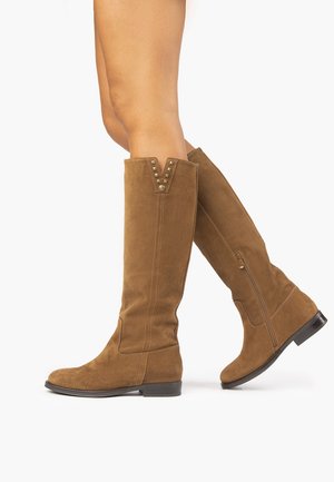 Kahvat ruskeat mokkasaappaat, joissa on V-muotoinen leikkaus, niitit ja sivuvetoketju. Sujuva pinta ja matala kanta.