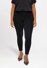 Czarne legginsy wykonane z elastycznego materiału o gładkiej fakturze, w połączeniu z czarną satynową bluzką i szpilkami w z wzorem panterki.