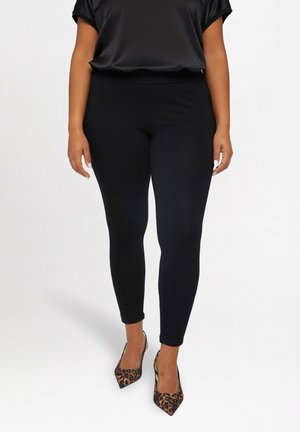 Zwarte leggings van rekbaar materiaal met een gladde textuur, gecombineerd met een zwart satijnen top en hoge hakken met luipaardprint.