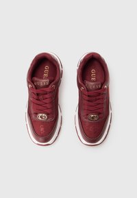 Une paire de baskets bordeaux Guess avec des détails en maille et en cuir, un logo doré sur les languettes et les lacets, des semelles intermédiaires blanches et des semelles d'usure à motifs.