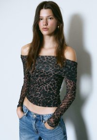 Sort mesh langærmet top med leopardprint, off-the-shoulder design, rynkedetaljer og tætsiddende silhuet, parret med blå jeans.