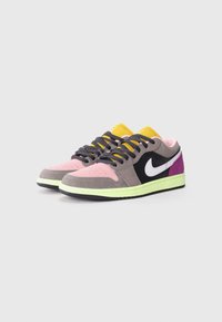 Lage sneakers in grijs, roze en zwart suède met een witte Nike swoosh, gele accenten, groene tussenzool en zwarte rubberen buitenzool.