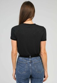 T-shirt noir à manches courtes avec un col rond, associé à un jean en denim bleu taille haute avec poches arrière et une finition délavée.