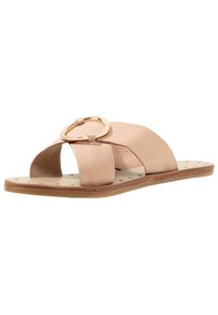 Sandale slide en cuir beige avec larges brides croisées et grande boucle ovale dorée sur semelle plate avec petits clous dorés.