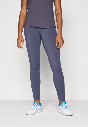 Gray athletic leggings with a smooth texture, form-fitting design, and ankle length, paired with white and blue sneakers.