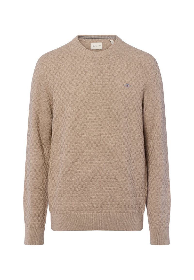 Beżowy sweter z dzianiny z teksturowanym wzorem, okrągłym dekoltem i ściągaczami na rękawach. Mały akcent w postaci logo na klatce piersiowej.