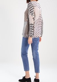 Blusa a maniche lunghe con una combinazione di motivi a pois grandi e piccoli in beige, nero e bianco. Abbinata a jeans in denim blu e scarpe nere.