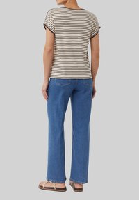 Gestreiftes beige und braunes T-Shirt mit kurzen Ärmeln, kombiniert mit blauen, geraden Jeans und beigen Flip-Flops. Lässig, entspannt geschnitten.