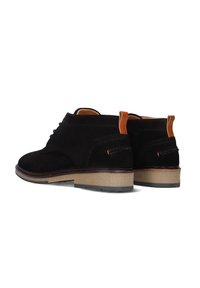 Zwarte suède schoenen met een ronde neus, een bruine rubberen zool en een tan treklus aan de hiel. Subtiele stiksel details aan de zijkanten.