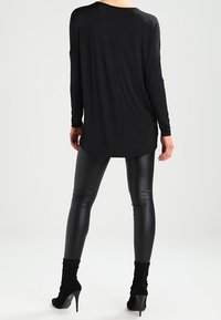 Schwarzes Langarmoberteil, lockere Passform, weicher Stoff. Kombiniert mit glänzenden schwarzen Leggings und hohen Stiefeletten, die eine elegante Silhouette schaffen.