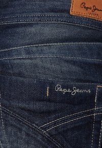 Mörkblå denimjeans med synlig sömnad, en läderlapp märkt "Pepe Jeans" och en subtil broderad logo på bakfickan.