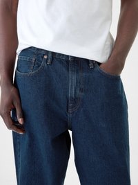 Vaqueros de mezclilla azul oscuro con un corte holgado, con bolsillos frontales, cremallera y costuras en contraste. Material de algodón con una textura suave.