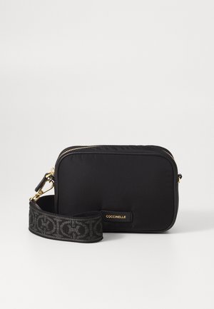 Sac bandoulière rectangulaire noir avec fermeture éclair dorée et sangle amovible de marque présentant un motif géométrique et une étiquette "COCCINELLE".