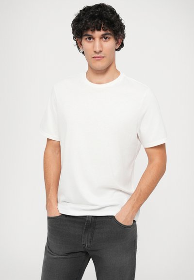 T-shirt branca de gola redonda em tecido suave, com mangas curtas, combinada com jeans cinza escuro; textura suave, ajuste descontraído, design minimalista.