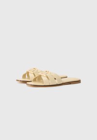 Light yellow slides with three wide straps and a gold-tone decorative accent. Flat sole, smooth texture, and minimalist design.