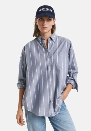 Chemise à rayures bleu clair avec des manches longues et une poche avant, associée à une casquette bleu marine avec des lettres blanches. Coupe décontractée.