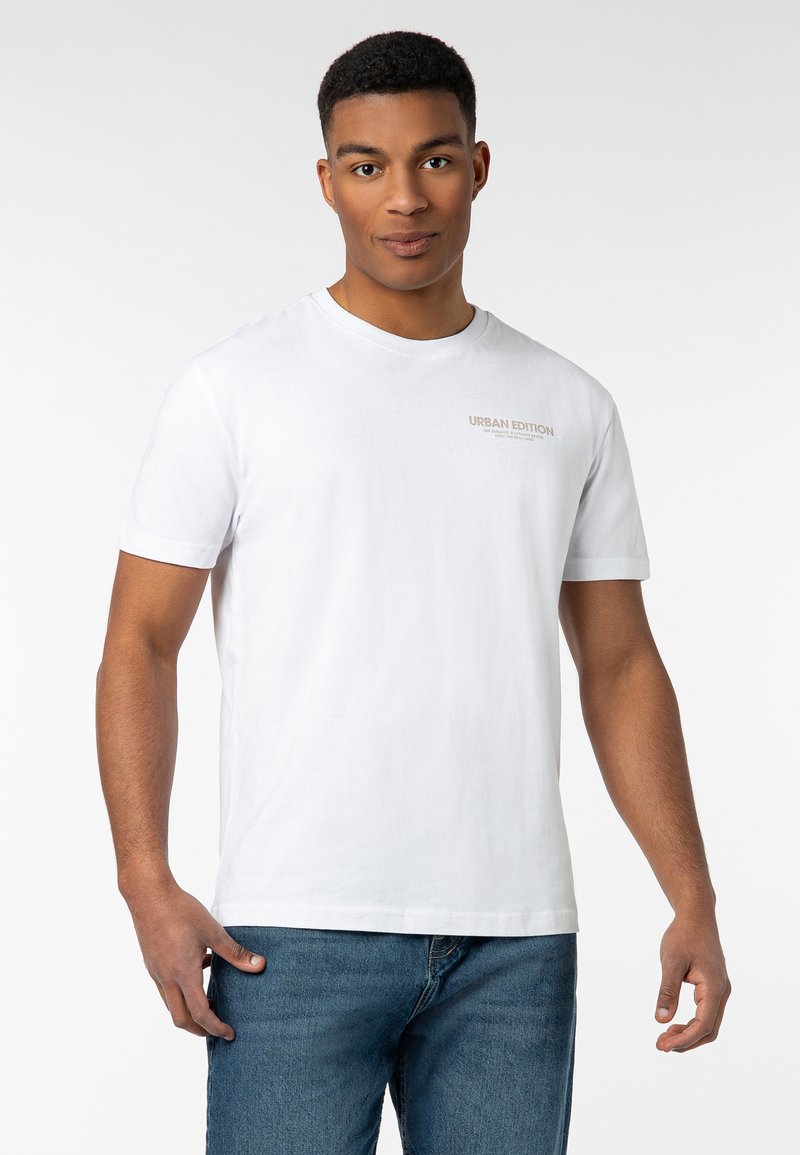 Weißes Baumwoll-T-Shirt mit Rundhalsausschnitt und kurzen Ärmeln, mit dezentem "URBAN EDITION"-Text auf der Brust. Kombiniert mit blauen Jeans.