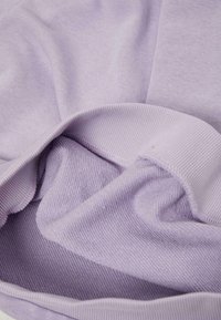Helllila Stoff mit weicher Textur, der gerippte und glatte Abschnitte zeigt, gefaltet, um unterschiedliche Webmuster und Dicken zu enthüllen.