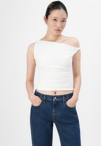Hvit, kort, en-skulder topp med samlet tekstur; sammen med høyt liv, mørke denimjeans med sidelommer og knappelukking.