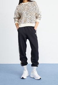 Leopardmönstrad sweatshirt i beige och svart, kombinerad med svarta joggingsbyxor med sidostripes och vita sneakers.