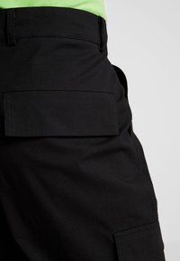 Black cargo shorts featuring large side pockets and a smooth texture. The fabric has a slightly coarse appearance with reinforced stitching.