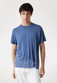 Camiseta de manga corta azul hecha de tela suave, con un patrón de cachemira en la mitad inferior y un cuello redondo. Textura suave.