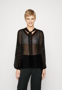 Svart gjennomsiktig bluse med fargerike broderte prikker, lange ermer og nøkkelhull-halslinje. Har plisserte detaljer og myk tekstur.