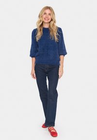 Mörkblå fluffig tröja med trekvartsärmar, kombinerad med mörka jeans och röda ballerinas. Slät textur, avslappnad passform.