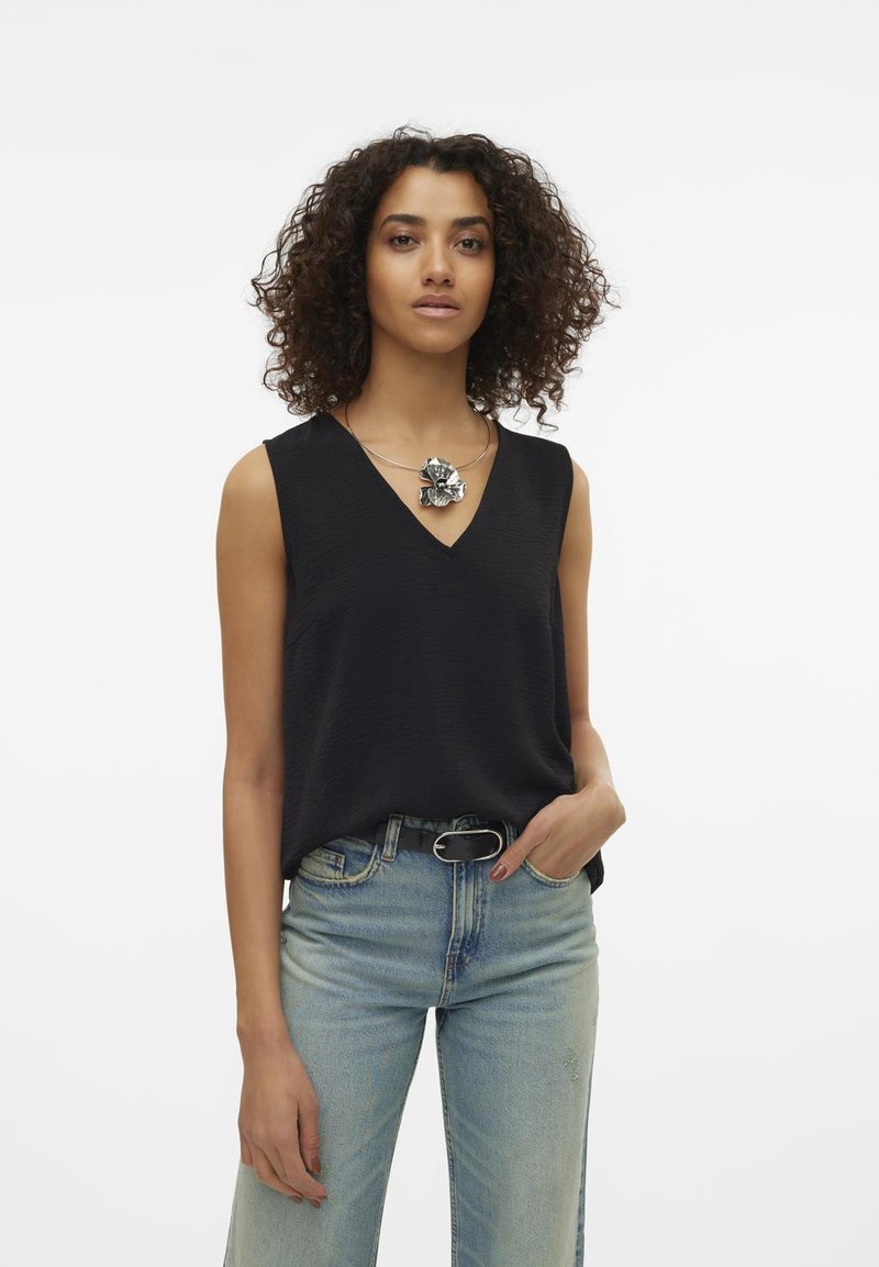 Black sleeveless top with a V-neck design, textured fabric, paired with light blue high-waisted jeans. Model wears a decorative silver necklace.