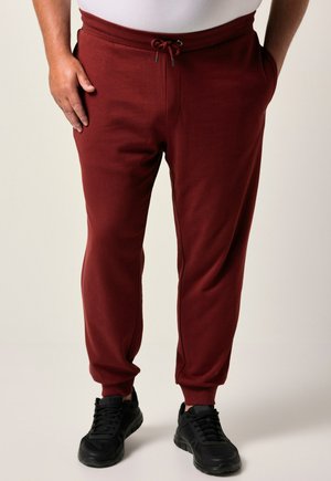Bordeauxfarbene Sweatpants mit Kordelzugbund, seitlichen Taschen und schmal zulaufenden Säumen, kombiniert mit schwarzen Sportschuhen. Baumwollmischmaterial.