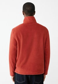 Rote Fleecejacke mit hohem Kragen und langen Ärmeln, mit einer weichen Textur und einem lässigen Schnitt. Die Rückansicht zeigt ein einfaches Design.