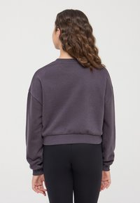 Fioletowa krótka bluzka z ribbowanymi mankietami i dołem. Miękki materiał o luźnym kroju i opadających ramionach. Gładki design, bez widocznych wzorów.