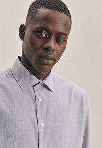 Kraagloze, knopenoverhemd met dunne blauwe en witte verticale strepen. De stof lijkt lichtgewicht met een soepele textuur.