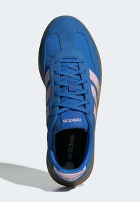 Plavi atletski tenisice s gornjim dijelom od suknje i mrežasti materijal, s ružičastim prugama, okruglim vrhom i smešnim gumiranim đonom. Brendiranje je vidljivo na jeziku.