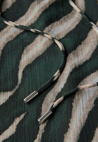Tessuto a righe verdi e beige con una superficie textured. Presenta due cavi con punte metalliche argentate. Il motivo ricorda una stampa animale.