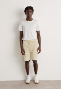 Light gray t-shirt paired with beige drawstring shorts. Model wears white sneakers with beige soles. Simple design, relaxed fit.
