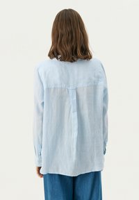 Camicia azzurro chiaro con colletto, maniche lunghe e taglio morbido, realizzata in un tessuto soffice. Presenta un dettaglio con yoke posteriore e polsini abbottonati.